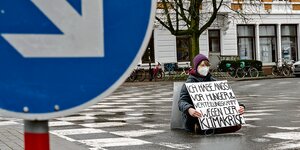 Aktivistin Lynn sitzt auf einer Straße mit einem Schild auf dem steht: "Ich habe Angst vor Hunger und Verteilungskampf wegen der Klimakrise".