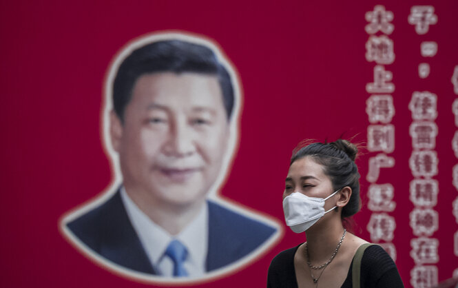 Eine Frau mit Atemschutzmaske geht an einem Bild des chinesischen Staatschefs Xi Jinping vorbei