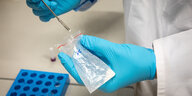 Hände in blauen Laborhandschuhen halten ein Plastiktütchen mit einer weißen Substanz