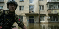 Ein Mann in Unifrom vor einem Mietshaus, das überflutet ist