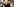 Porträt Claudia Roth, dunkler Pulli, Brille, lächelt und gestikuliert mit Händen vor Regalwand