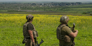Zwei Soldaten gucken von einer Erhebung über ein Feld und eine Stadt