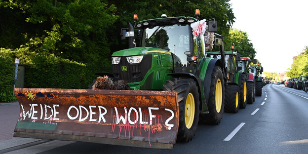 "Weide oderWolf?" steht auf der Schaufel des ersten Fahrzeugs einer Treckerkolonnne