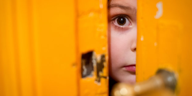 Kind schaut ängstlich durch Türspalte.