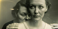 Zwei Frauen auf einem Bild. Die Frau im Vordergrund guckt mit leichter Anspannung seitlich nach vorne. Eine Frau hinter ihr drückt ihr melancholiisch wirkendes Gesicht auf ihre Schultern.