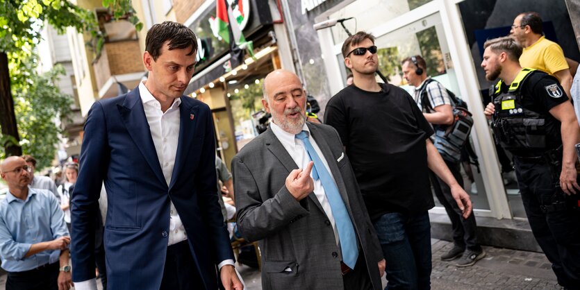 Martin Hikel und Ron Prosor umgeben von Sicherheitsbeamten auf der Sonnenallee