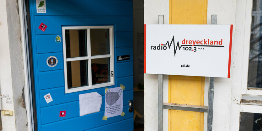 Eine offene Tür mit Aufklebern, daneben ein Schild von Radio Dreyeckland