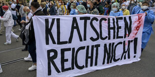 Auf einer Demo halten Menschen ein Transparent mit der Aufschrift "Klatschen reicht nicht" hoch