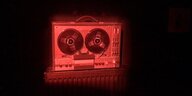 Ein rot ausgeleuchtetes analoges Tonband, wie es auch die Stasi benutzte