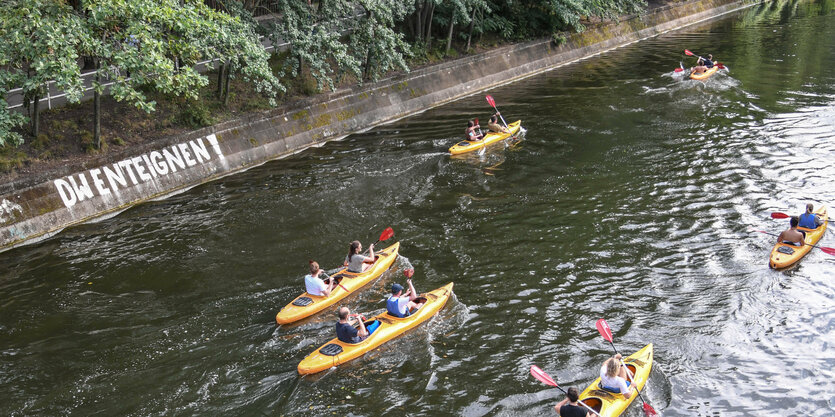 Menschen fahren in Kanus auf dem Berliner Landwehrkanal. An der Kanalwand ist ein Graffiti mit den Worten "DW ENTEIGNEN!"