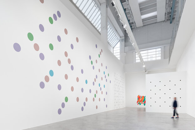 Raumansicht der Ausstellung „Wall Works 1983–2023“ von Bridget Riley in den Galerieräumen von Max Hetzler. Die linke, hohe Wand ist mit Kreisen aus lila und grünen Pastellfarben übersät, die direkt auf die Wand aufgetragen wurden.