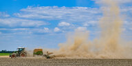Ein Traktor wirbelt auf einem Feld viel Staub auf