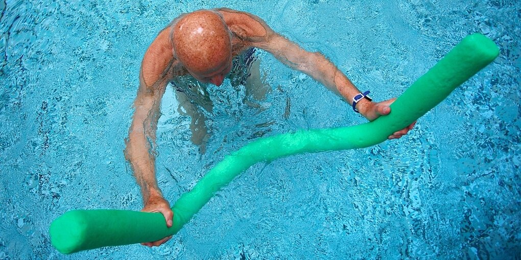 Alter Mann im Schwimmbecken, der eine Schwimmnudel hält, von oben fotografiert