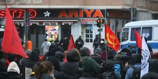 Eine Kundgebung auf der Straße vor einer unscheinbar aussehenden Kneipe, vor der Polizisten stehen