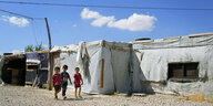Drei kleine syrische Kinder gehen an ihren Familienzelten vorbei