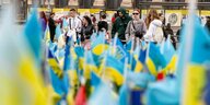 Passanten stehen vor ukrainischen Fähnchen, die in die Erde gesteckt wurden