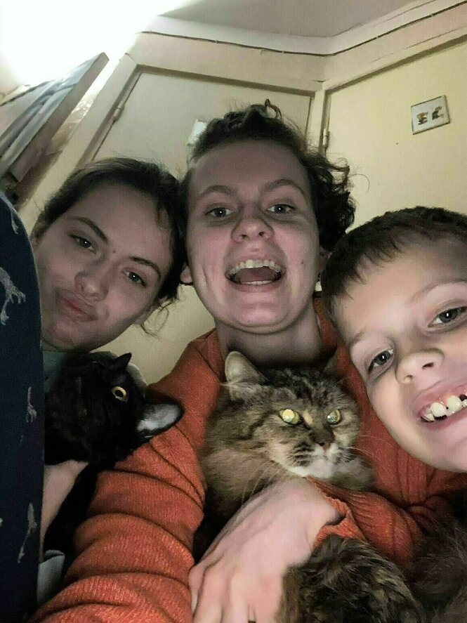 Selfie von drei lachenden Jugendlichen in einer Wohnung, die beiden Mädchen halten jeweils eine Katze im Arm