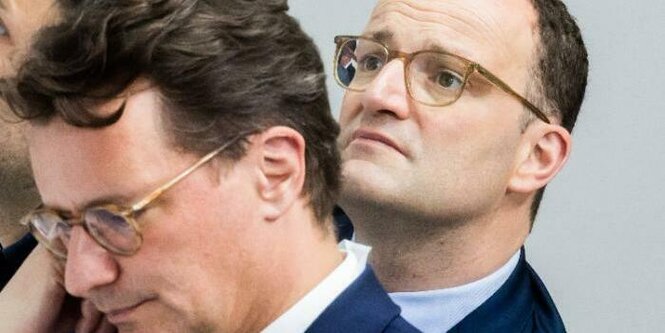 Hendrik Wüst und Jens Spahn neigen die Köpfe in entgegengesetzte Richtungen