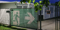 Ein Transparent mit dem Symbol für den Fluchtweg hängt vor Wohncontainer