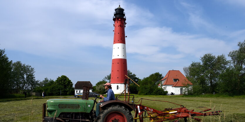 Im Vordergrund ein Traktor auf einer grünen Wiese, im Hintergrund ein weiß-rot geringelter Leuchtturm.