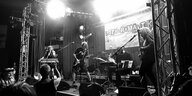 Schwarz-weiße Aufnahme von links nach rechts: Die Band Rosa Beton auf der Bühne: Martina Dünkelmann steht am Keyboard und singt, Thomas Wagner spielt E-Gitarre, Alexander Lode sitz an einem Drumcomputer, hinter ihm steht ein Schlagzeug, und Thomas Trenkel