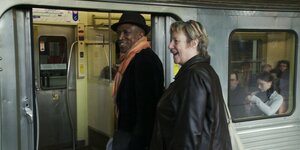 Ein Mann und eine Frau mittleren Alters stehen vor der geöffneten Tür, um in den Wagen einer S-Bahn zu steigen. Sie blicken nach links und lachen.