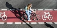Eine Radfarerin wirft einen Schatten, sie fährt auf einem roten Radweg von oben aufgenommen