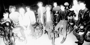Das Schwarzweißfoto ist stark überbelichtet, es zeigt eine Gruppe junger Männer in Stiefeln und Lederjacken vor ihren Motorrädern. Die Gesichter sind nicht zu erkennen.