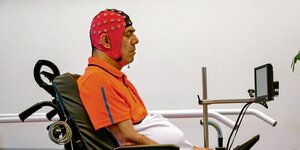 Ein Mann sitzt in einem Rollstuhl und trägt eine rote Kappe auf dem Kopf