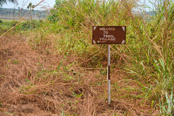 Ein verrostetes kleines Schild mit der Aufschrfit Welcome to Tonka Village steht im Gestrüpp