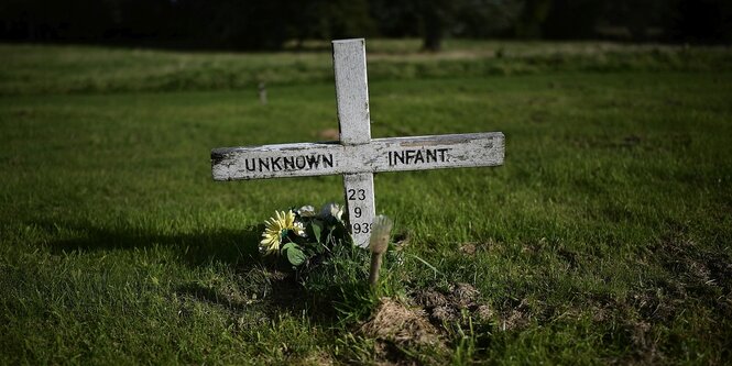 Ein Holzkreuz auf grünem Rasen. Auf dem Kreuz steht geschrieben "Unknoen Infant"