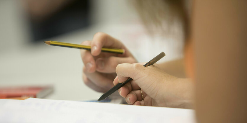 Eine Kinderhand hält einen Stift, eine Erwachsenenhand ebenso