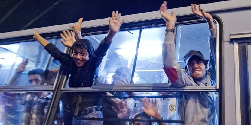 Menschen lehnen sich aus einem Busfenster und jubeln