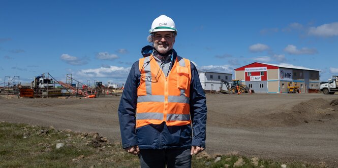 Ein mann mit Schutzweste und Arbeitshelm steht vor einer Baustelle