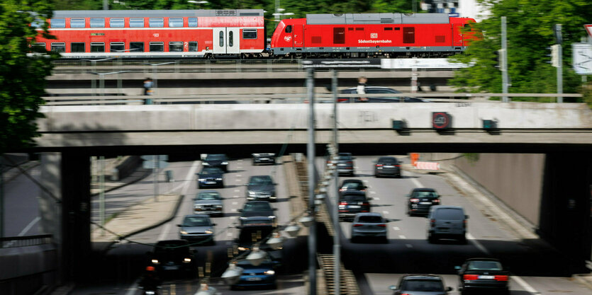 Eine rote Bahn fährt über eine Brücke, darunter fließt vierspurig der dichte Autoverkehr