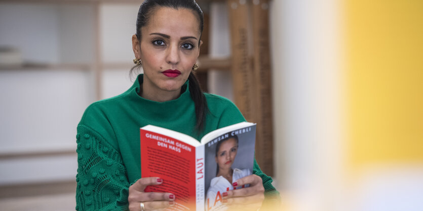 Sawsan Chebli sitzt auf einer Treppe und hält ihr Buch "Laut" in den Händen. Sie schaut ernst in die Kamera.