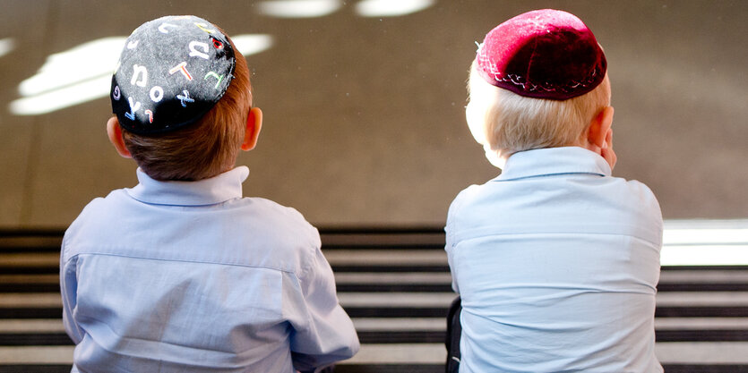 Zwei Kinder mit Kippas sitzen auf einer Treppe, sie sind von hinten fotografiert