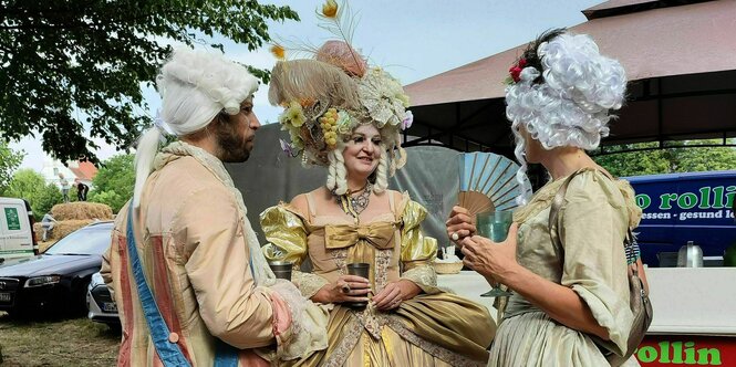 Drei Menschen in barocken Kostümen machen Konversation