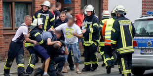 Mehrere Feuerwehrleute ringen mit augenscheinlich aggressiven Anwohnern.