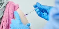 Eine Corona-Impfspritze wird in einen Oberarm gesetzt