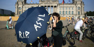 Personen vor dem Gebäude des Bundestags halten einen Regenschirm mit der Aufschrift "R.I.P. ASYL"