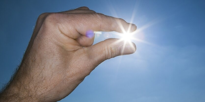 Es sieht so aus als wenn zwei Finger eine strahlende Sonne halten würden