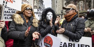 Menschen protestieren, sie klatschen in die Hände und hlten SChilder, eine Person trägt eine weiße Maske