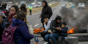 Mehrere Menschen, darunter auch ein Kind, blockieren mit brennenden Autoreifen eine Straße, im Hintergrund stauen sich Autos