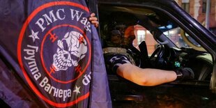 Ein Soldat sitzt im Auto. Vor dem Auto wird eine Flagge ins Bild gehalten