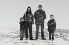 Mutter, Vater, zwei Kinder stehen in Winterjacken auf einem verschneiten Feld