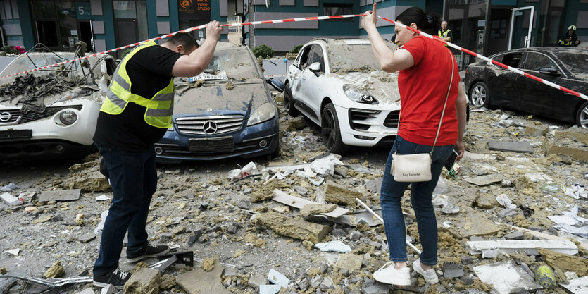 Zwei Männer ducken sich vor unter Schutt begrabenen Autos unter einem Absperrband hindurch