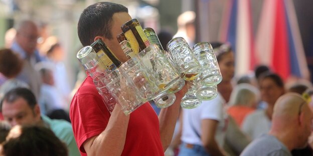 Ein Kellener trägt schwer an Flaschen und Gläsern