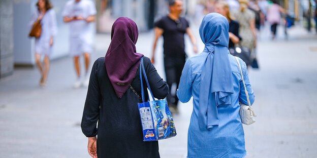 Zwei Frauen mit Kopftüchern gehen eine Straße entlang