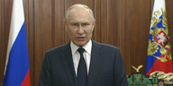 Präsident Wladimir Putin steht zwischen zwei russischen Flaggen und spricht in die Kamera